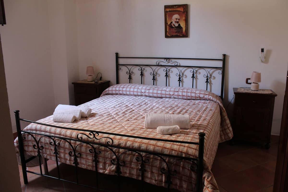 A neatly made bed with a checkered bedspread and two towels, a bedside table with a lamp, and a wall-mounted picture.