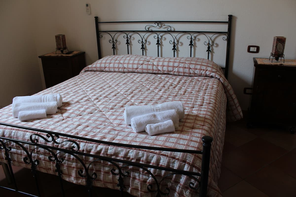 A neatly made bed with a checkered bedspread and two rolled towels on the bed.