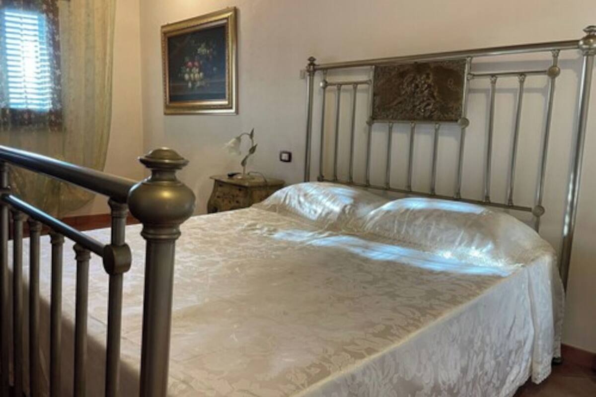 A bedroom with a metal bed frame, a wooden headboard, a nightstand, and a window with curtains.