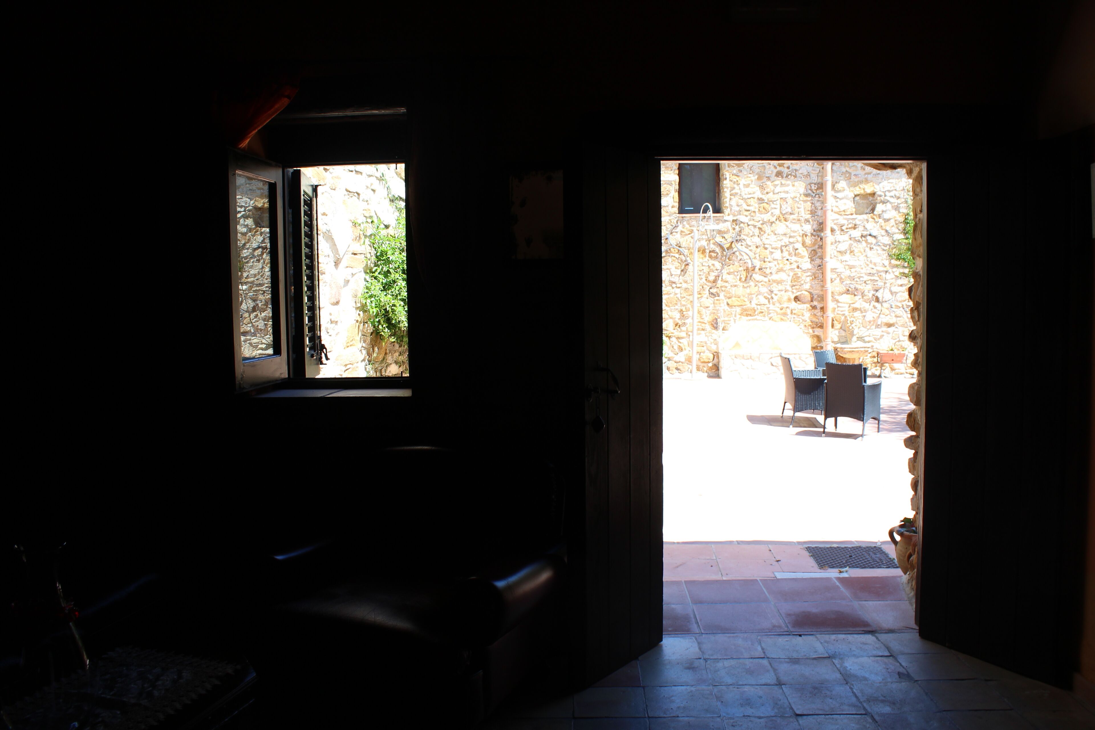 Un umbral abierto que da a un patio al aire libre con un muro de piedra y una mesa y una silla.
