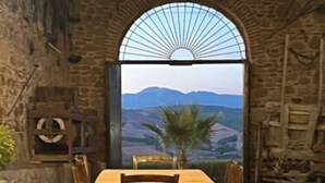 Un comedor con pared de piedra y vista a montañas a través de un amplio ventanal en arco.