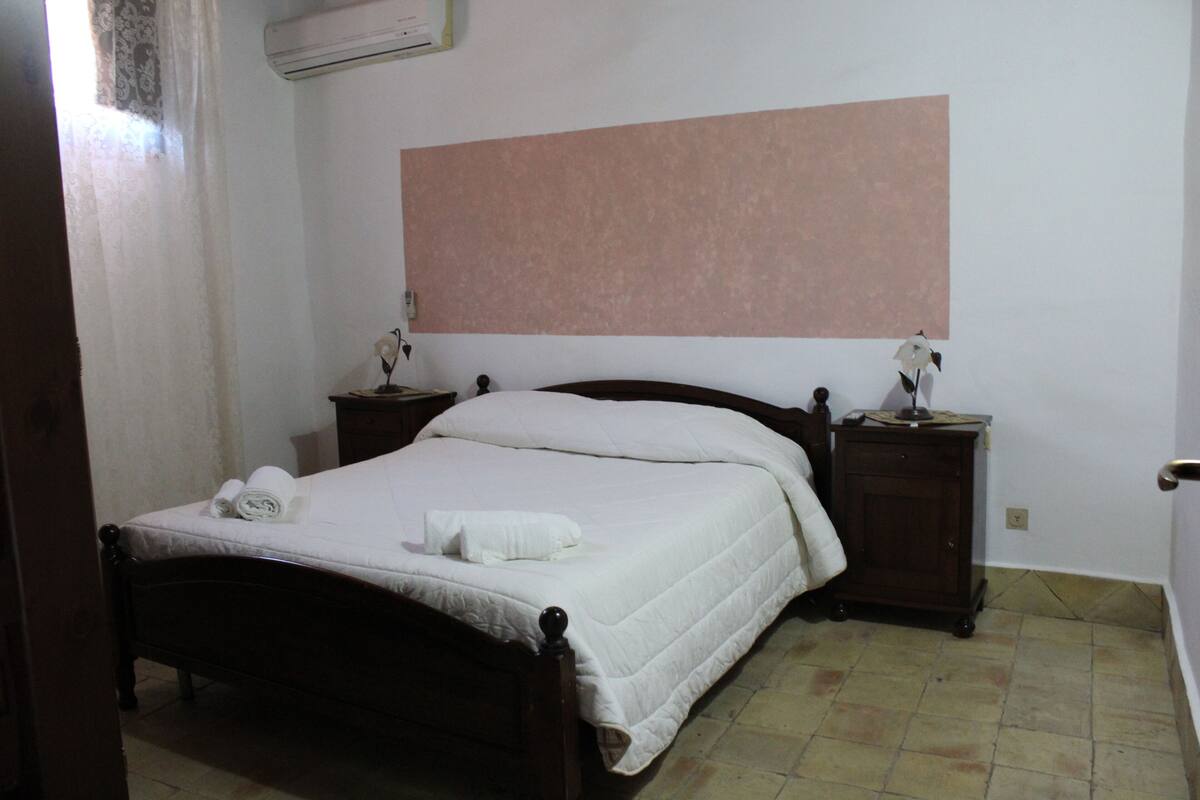 A bedroom with a bed, two bedside tables, and a wall-mounted air conditioner.
