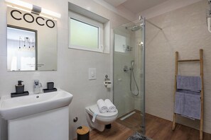 Et moderne badeværelse med bruseniche, toilet, håndvask og et håndklædestativ.