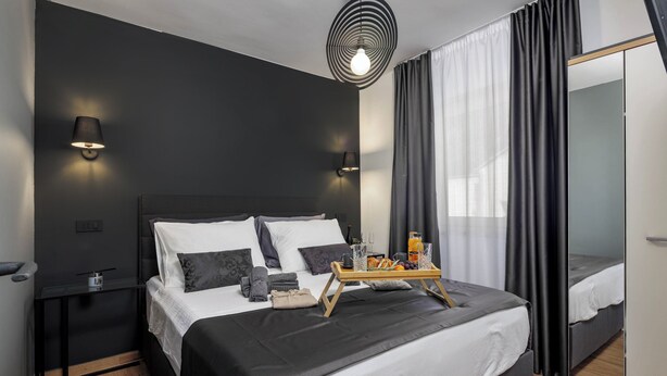 Une chambre moderne avec un grand lit, des tables de chevet, un miroir et un plateau contenant des éléments pour le petit-déjeuner.
