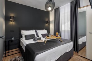 Et moderne soveværelse med en stor seng, sengeborde, et spejl og en bakke med frugt og en flaske.