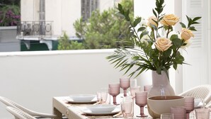 Et spisebord dækket med hvide tallerkener, lyserøde glas og en vase med blomster.