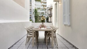 Spiseområde med et bord dækket til seks personer, omgivet af fletstole på en flisegulv med geometrisk mønster.