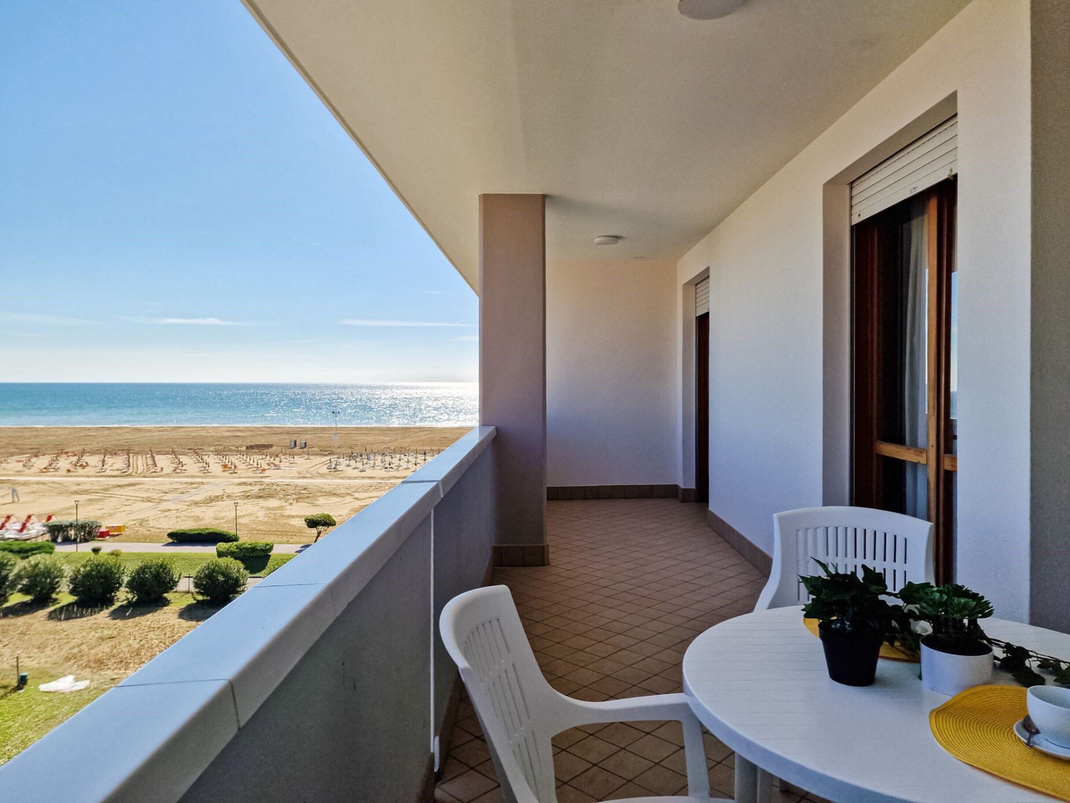 Un balcón con vistas a la playa, una mesa con sillas y plantas en macetas.