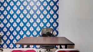 A conference room with a wooden table and chairs, a patterned wallpaper, and a plain white wall. - Hotel O Raya Guest House Syariah (Pekanbaru)