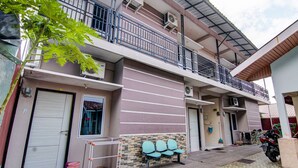 A two-story building with a balcony, air conditioning units, and a row of blue chairs outside. - Hotel O Raya Guest House Syariah (Pekanbaru)