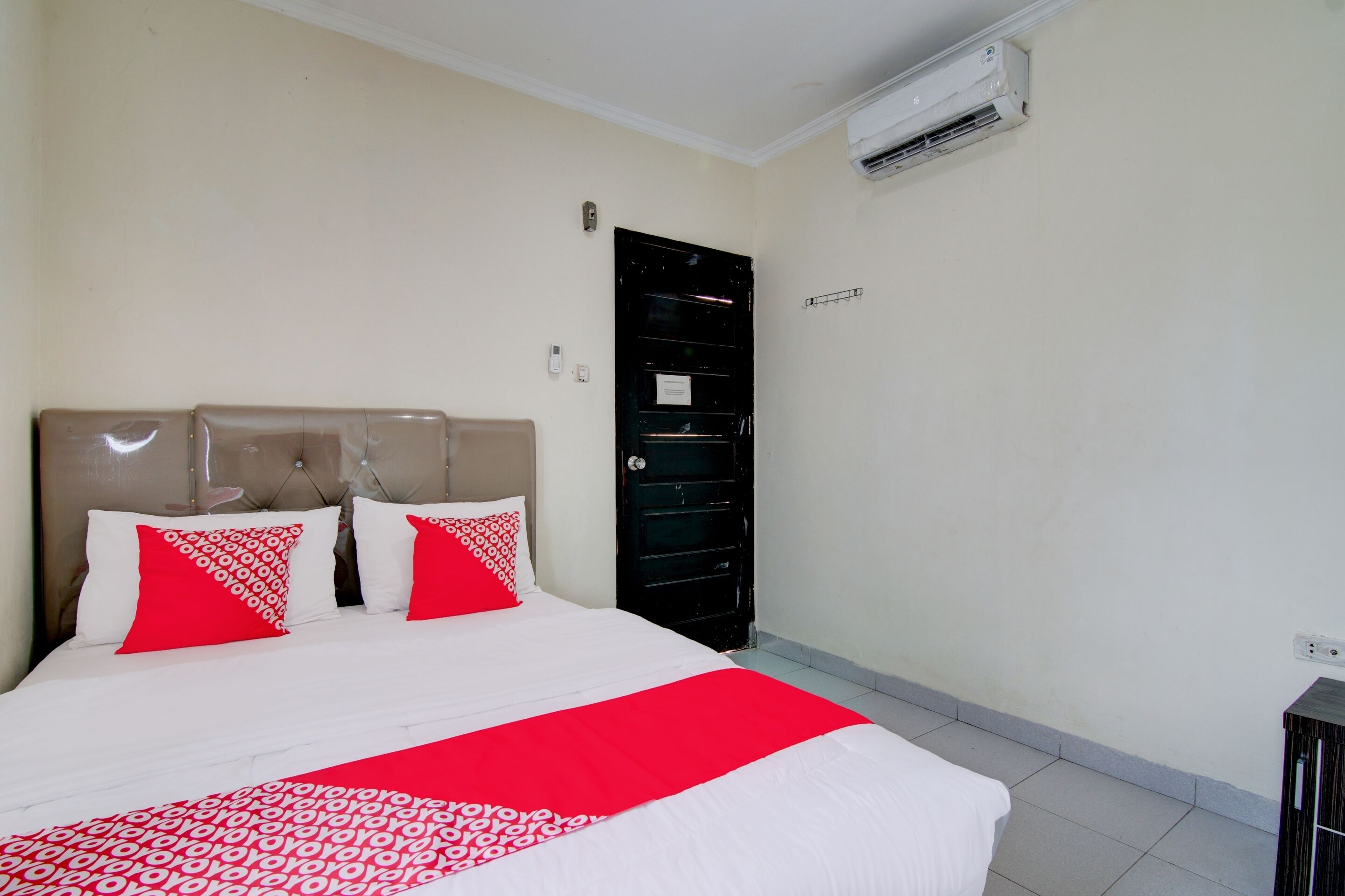 Quarto de hotel com uma cama, um guarda-roupa preto e um aparelho de ar condicionado na parede.
