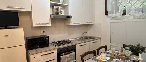 Een kleine keuken met witte kastjes, een gasfornuis, een magnetron en een ontbijttafel.