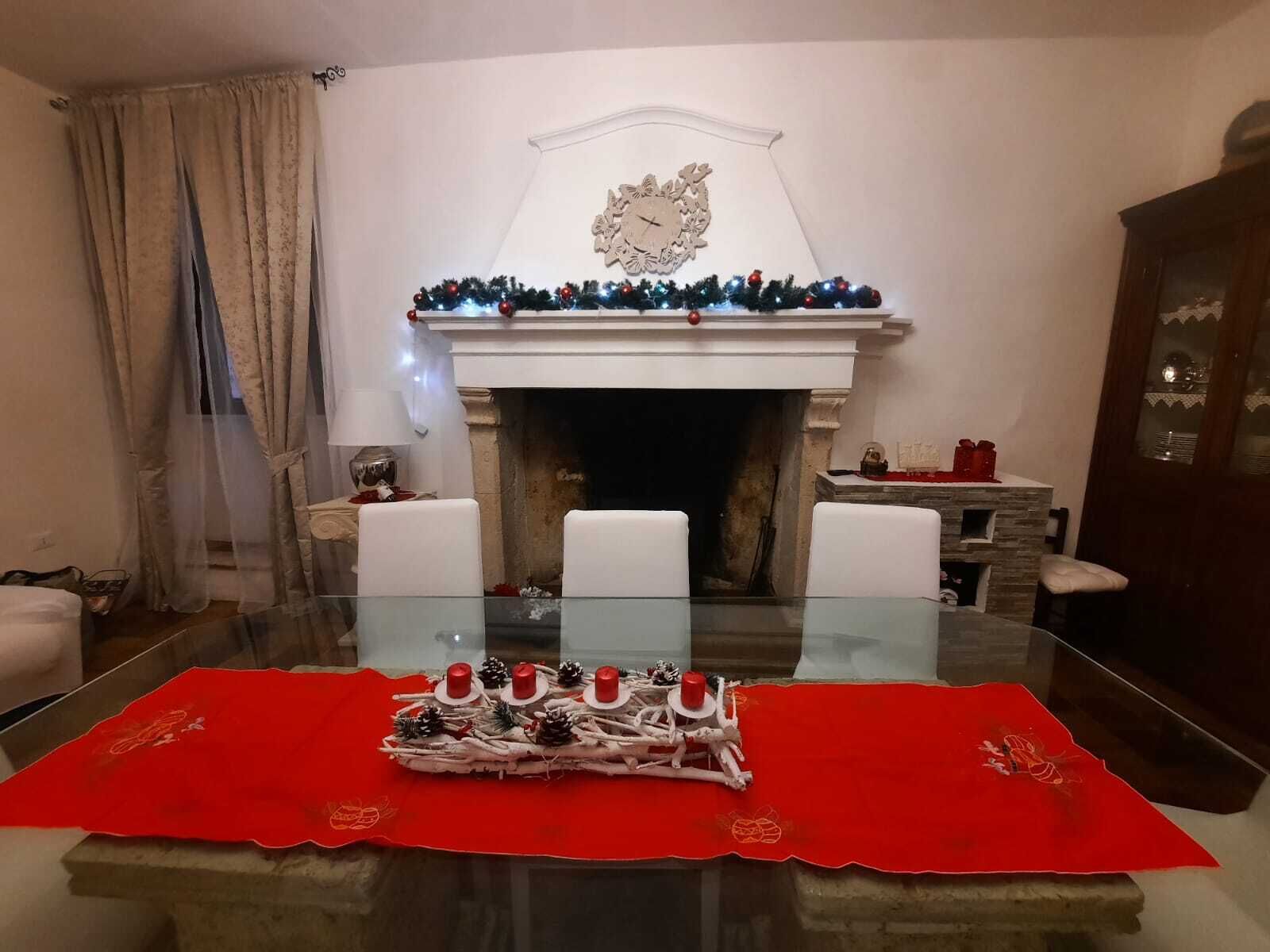 Een eetkamer met een glazen tafel, een rode tafelkleed en een open haard versierd voor Kerstmis.