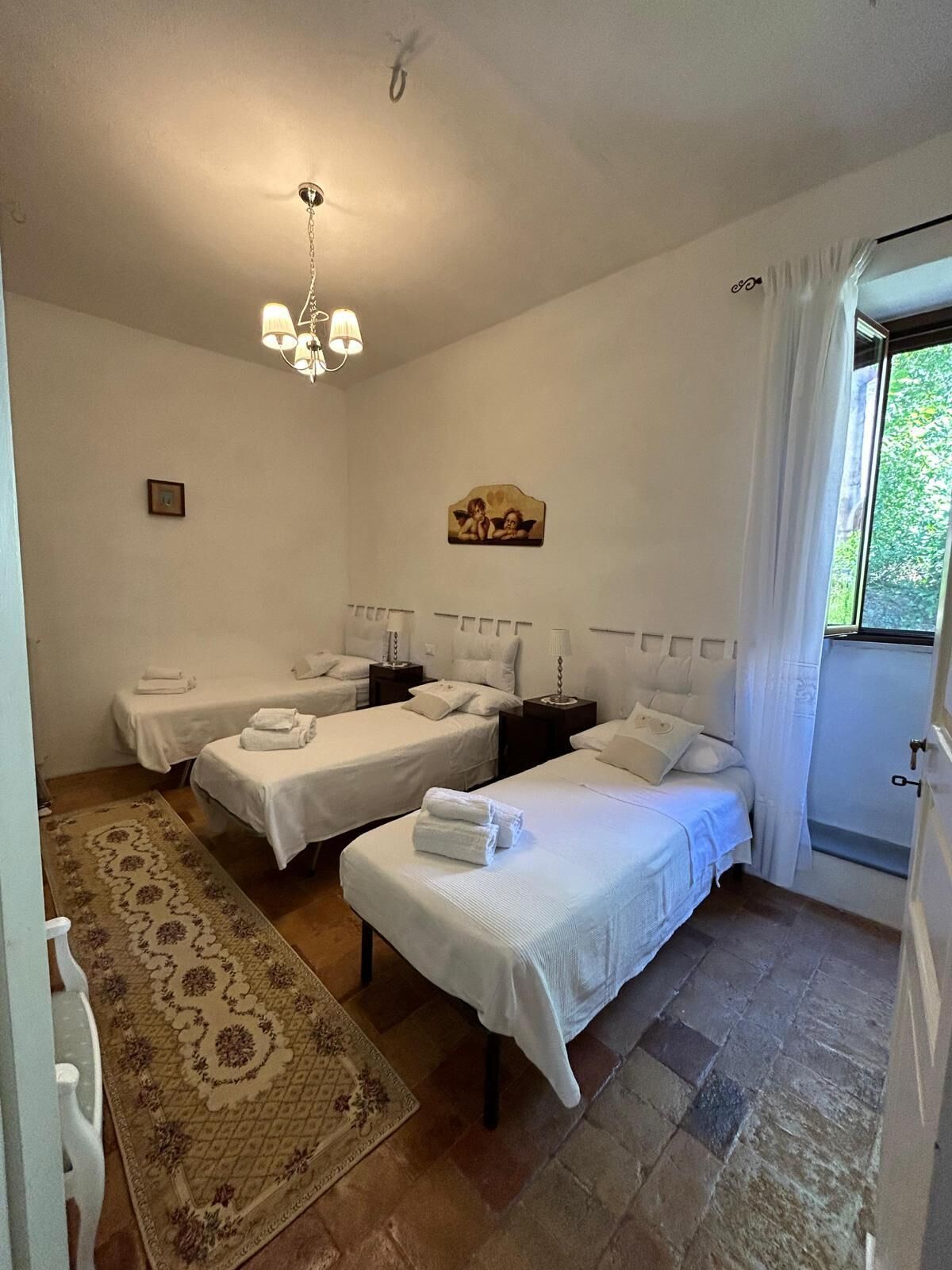 A hotel room with two single beds, a chandelier, a painting, and a window with curtains.