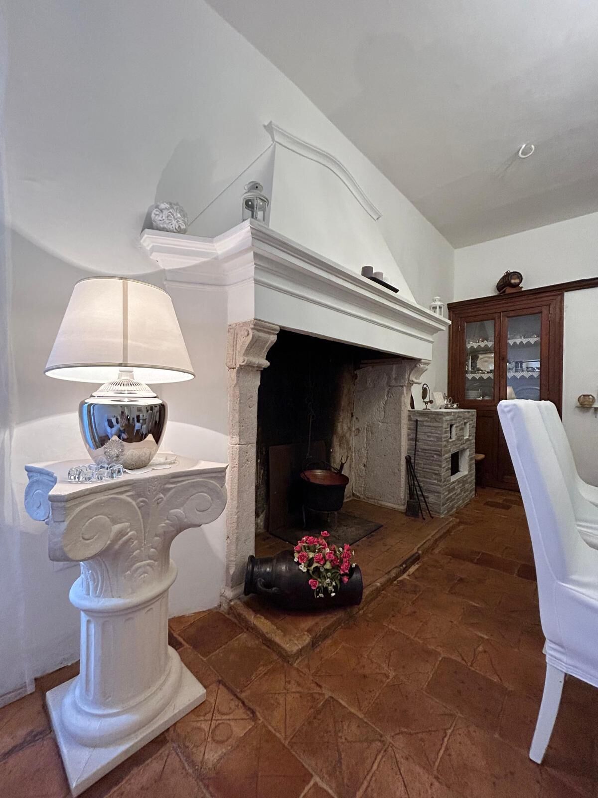 A room with a fireplace, a white chair, and a table with a lamp.