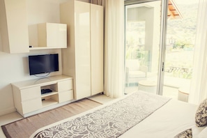 Une chambre à coucher comprenant un lit, une télévision, une armoire et une porte-fenêtre coulissante donnant sur un balcon.