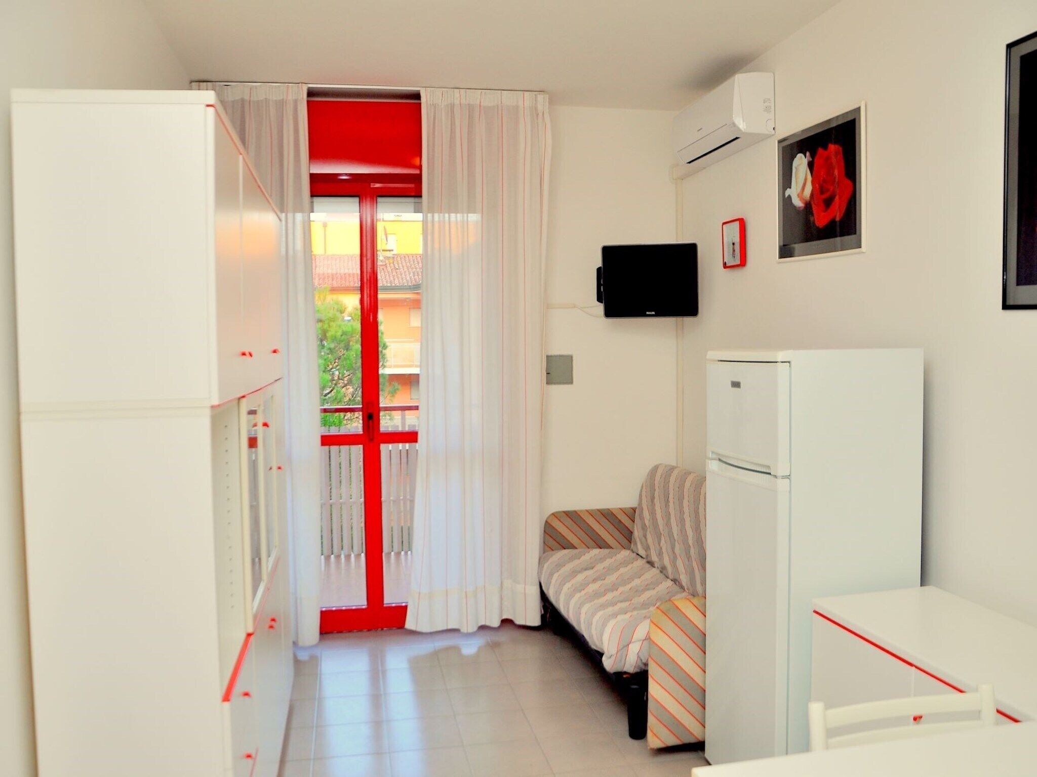 Ein kleines Zimmer mit Bett, Tisch, Fernseher und Kühlschrank.
