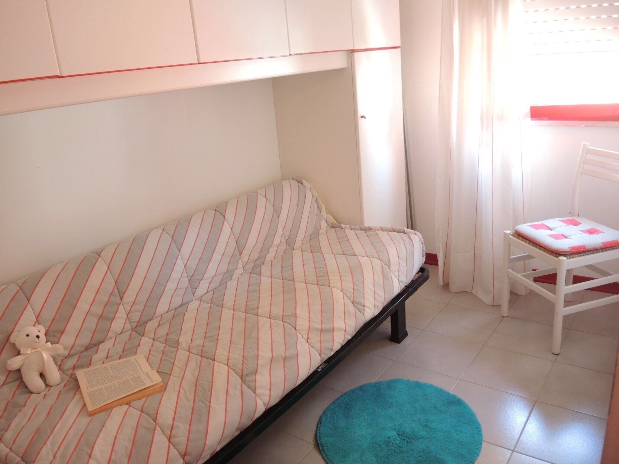 A room with a bed, a chair, a teddy bear, and a book.