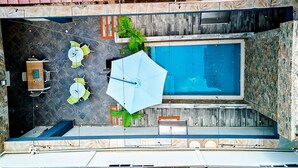 Vista aérea de un área de piscina en la azotea, con piscina, asientos y una sombrilla grande.