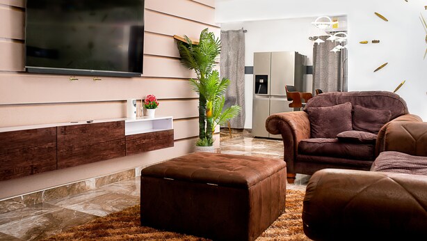 Una sala de estar moderna con un televisor de pantalla plana montado en la pared, un sofá de cuero marrón, un otoman a juego y una planta en maceta.