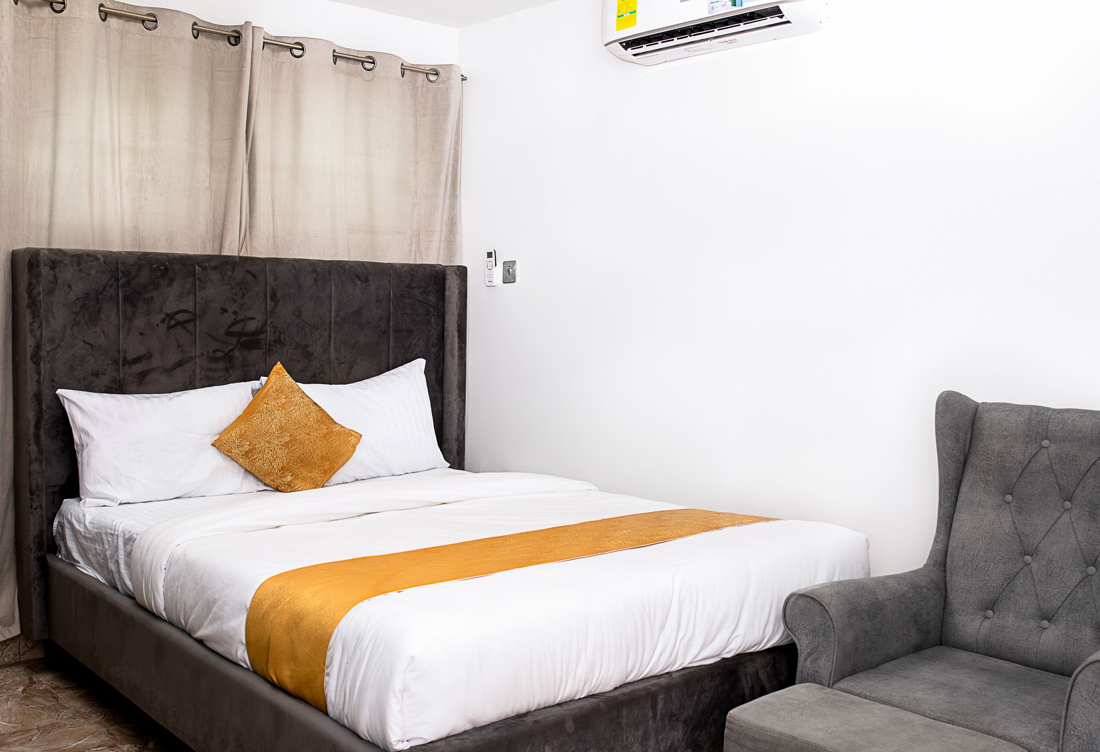 Een bed met een donker hoofdbord, witte beddengoed en een gouden plaid.