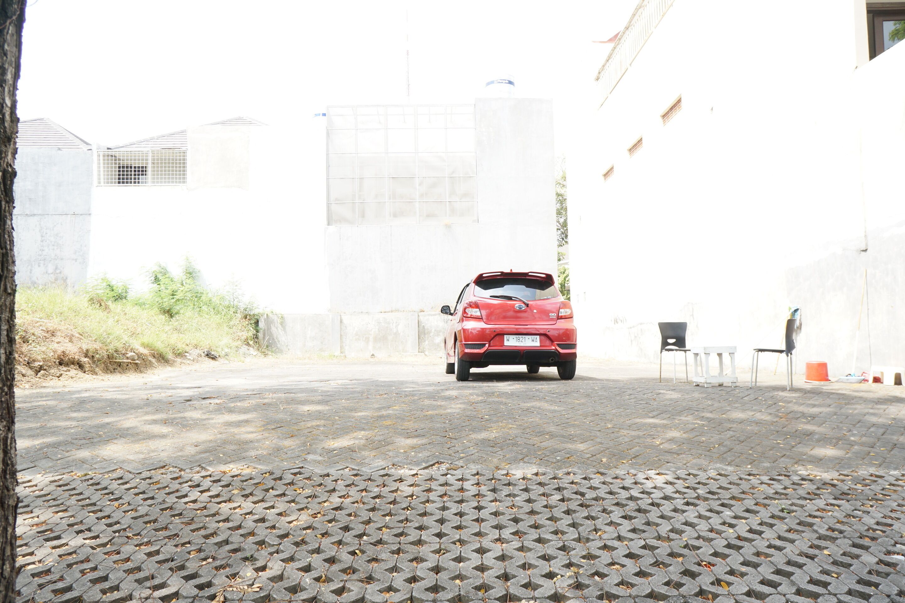 A red car parked on a paved area with a white building in the background.