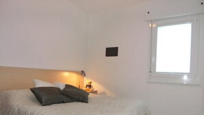 A bedroom with a bed, pillows, a bedside lamp, and a window. - Delightful Apartment in Bibione (San Michele al Tagliamento)