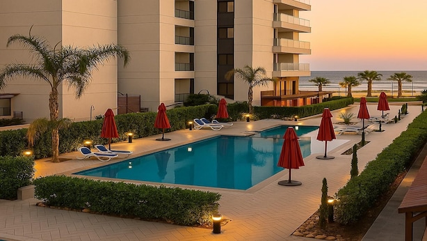 A pool area with lounge chairs and umbrellas, surrounded by a building with balconies and a view of the ocean. - Where Comfort Meets Elegance Porto Said Chalets (Port Said)