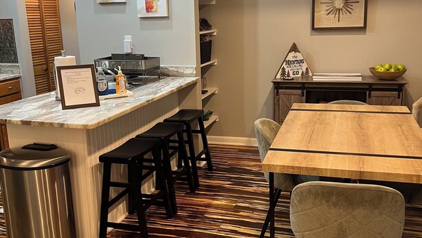 A modern kitchen with a marble countertop, black bar stools, and a wooden dining table. - Ski-In/Ski-Out Comfy Condo (Wintergreen)
