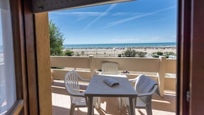 A balcony with a table and chairs, overlooking a beach with people and a clear sky. - Seaside Flat With Terrace - Beahost Rentals (San Michele al Tagliamento)