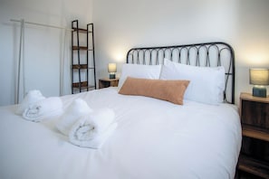A neatly made bed with white linens and rolled towels, a metal headboard, and bedside lamps on wooden nightstands. - Swn Y Mor - 4 Bedroom - Llanelli (Llanelli)