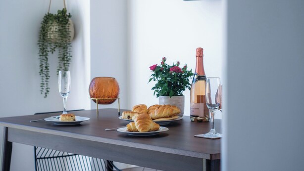 Une table à manger avec des croissants, une bouteille de champagne et un vase de fleurs.