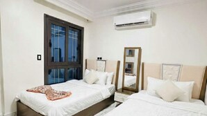 A hotel room with two beds, a window, an air conditioning unit, and a marble floor. - A Modern Haven Steps Away From the Beach (Al-Manasrah)