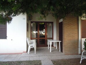 A patio with two white chairs and a table, a door with glass panels, and a brick wall. - Peaceful Villa With Garden 500mt From the sea (San Michele al Tagliamento)