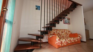 A staircase with wooden steps and black railings, a sofa with a floral pattern, and a small picture on the wall. - Terraced House With Garden and Porch (Rosolina)