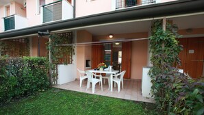 A patio with a table and chairs, surrounded by greenery and a building with a balcony. - Terraced House With Garden and Porch (Rosolina)