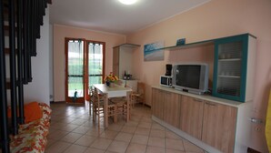 A compact kitchen with a dining table, chairs, a microwave, and a television. - Terraced House With Garden and Porch (Rosolina)