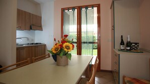 A kitchen with wooden cabinets, a dining table with a vase of sunflowers, and a view through a glass door. - Terraced House With Garden and Porch (Rosolina)