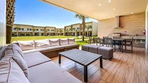 A modern outdoor living area with a sofa, a table, and chairs, overlooking a courtyard with a pool and buildings in the background.