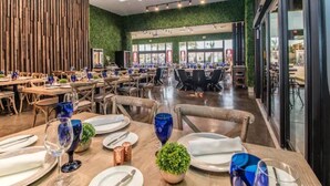 A spacious restaurant with multiple dining tables set for guests, featuring a modern design with wooden accents and green walls.