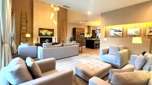 A modern living room with a sofa set, ottoman, and a dining area in the background.
