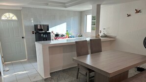 A modern kitchen with a central island, a dining area with a wooden table and chairs, and a white door with a window. - Villa 5 minutes from the sea with parking (Acapulco de Juárez)