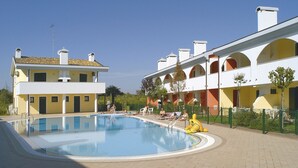 Ein Schwimmbeckenbereich mit Pool, Liegestühlen und einem Gebäude mit gelber Fassade und weißen Balkonen.