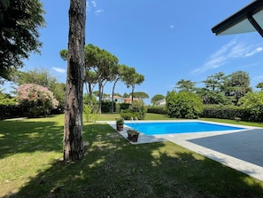 A swimming pool surrounded by a well-maintained lawn and trees.