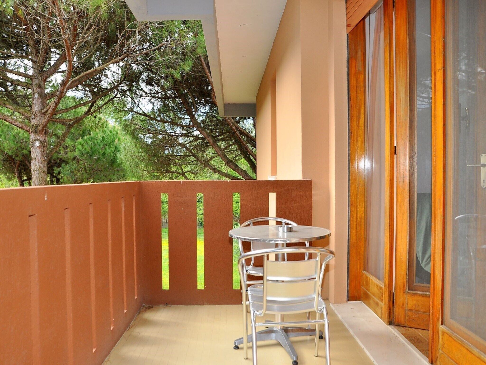 Ein Balkon mit Tisch und Stühlen, eine Holztür und Blick auf Bäume.