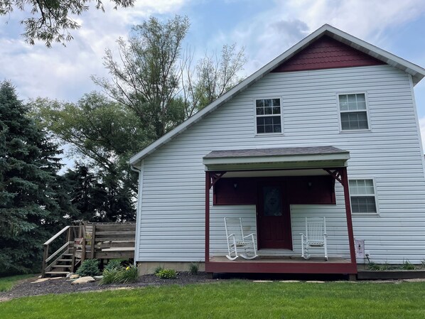 A white house with a red roof and a porch with white rocking chairs. - Charming farmhouse in a rural setting with an easy drive to Purdue (Wolcott)