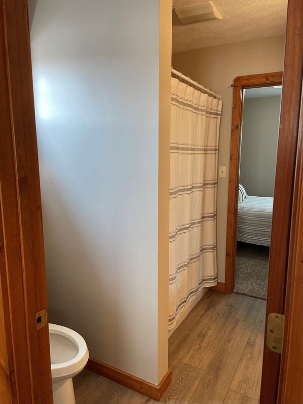 A narrow hallway with a toilet on the left, a shower curtain on the right, and a bed in the background. - Charming farmhouse in a rural setting with an easy drive to Purdue (Wolcott)