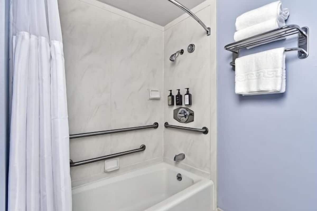 A shower area with a bathtub, handrails, a towel rack, and toiletries.