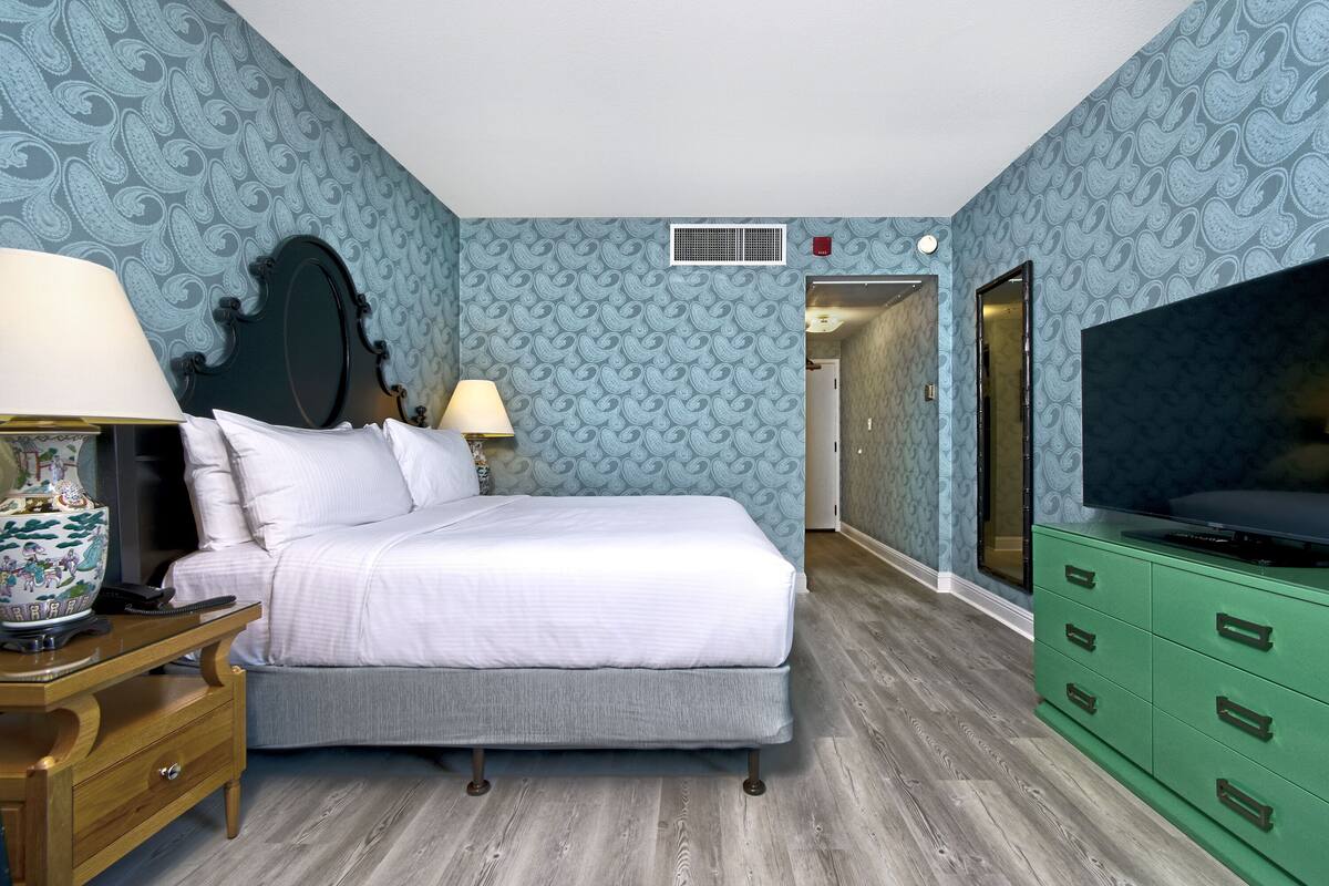A bedroom with a bed, bedside tables, a dresser, a television, and patterned wallpaper.