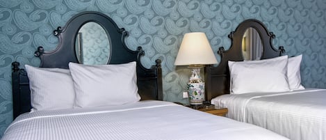 Una habitación de hotel con dos camas, una mesita de noche con lámpara y un papel tapiz estampado.
